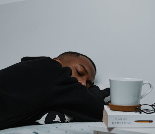 수면 혁명, ‘마이크로 슬립’부터 AI 수면 관리까지…최신 트렌드로 건강하게 자는 법 a man sleeping on a bed next to a stack of books